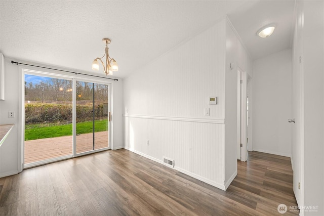 unfurnished dining area with a chandelier, visible vents, a textured ceiling, and wood finished floors