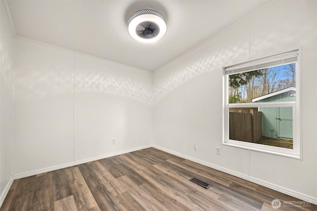 unfurnished room featuring baseboards, wood finished floors, visible vents, and ornamental molding