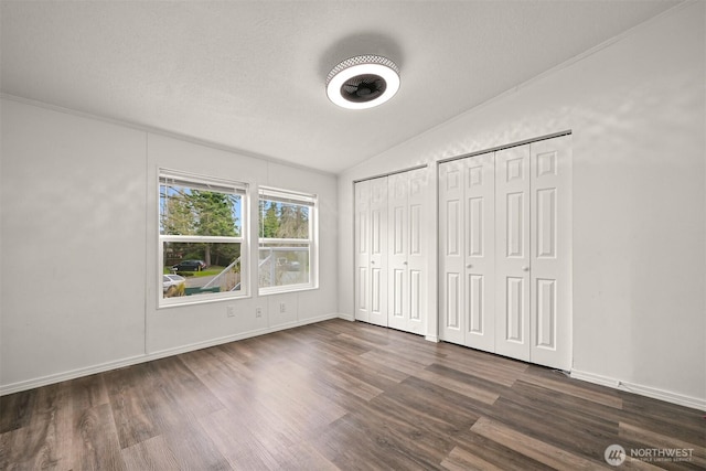 unfurnished bedroom with baseboards, lofted ceiling, dark wood-style flooring, a textured ceiling, and two closets