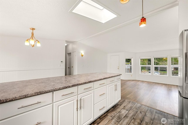 kitchen featuring pendant lighting, wood finished floors, freestanding refrigerator, vaulted ceiling with skylight, and white cabinets