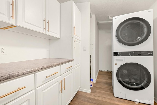 laundry room featuring light wood finished floors, cabinet space, stacked washer and clothes dryer, and a textured ceiling