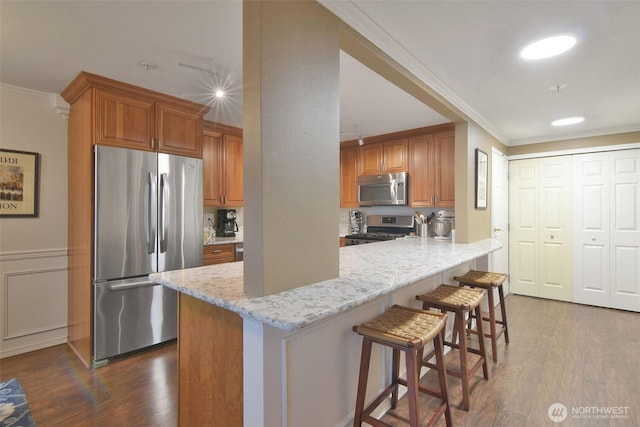 kitchen featuring appliances with stainless steel finishes, dark wood-style flooring, brown cabinetry, and light stone countertops