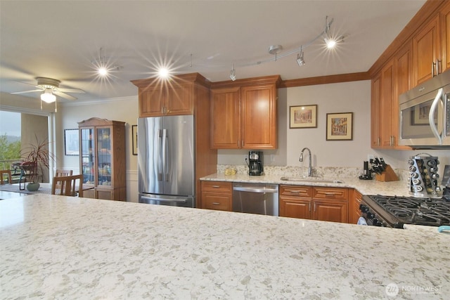 kitchen with light stone counters, stainless steel appliances, a sink, ornamental molding, and brown cabinets