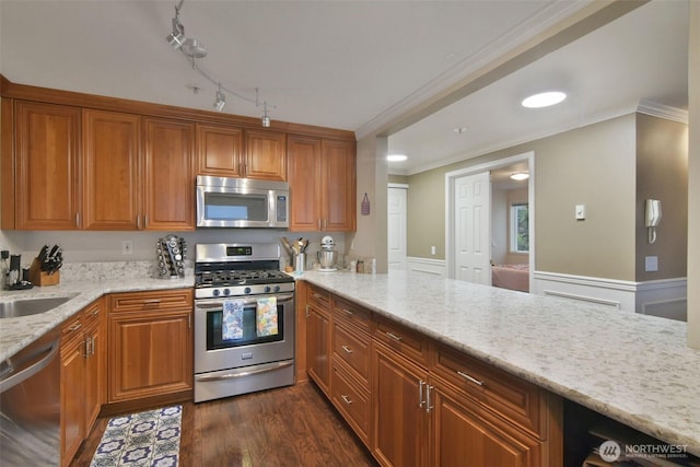 kitchen with appliances with stainless steel finishes, a sink, light stone countertops, and brown cabinets