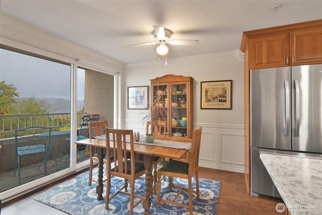 dining area featuring dark wood-style floors, a wainscoted wall, crown molding, and a ceiling fan