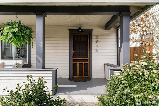 doorway to property featuring covered porch and fence