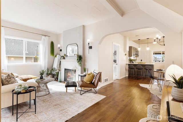 living room featuring visible vents, baseboards, hardwood / wood-style flooring, arched walkways, and a glass covered fireplace