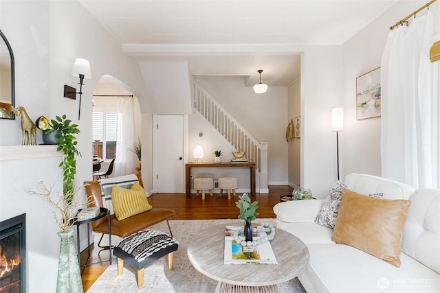 living area featuring a glass covered fireplace, stairway, and wood finished floors