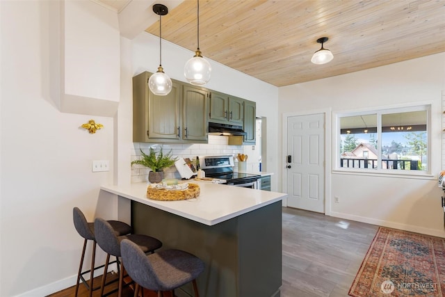 kitchen featuring under cabinet range hood, a breakfast bar, light countertops, decorative backsplash, and stainless steel electric range