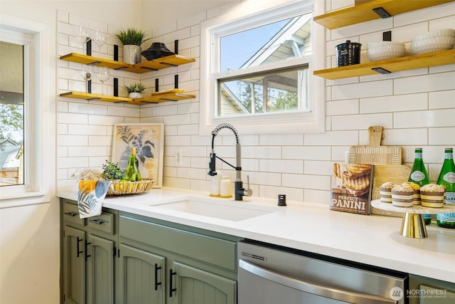 kitchen with green cabinetry, open shelves, a sink, stainless steel dishwasher, and backsplash