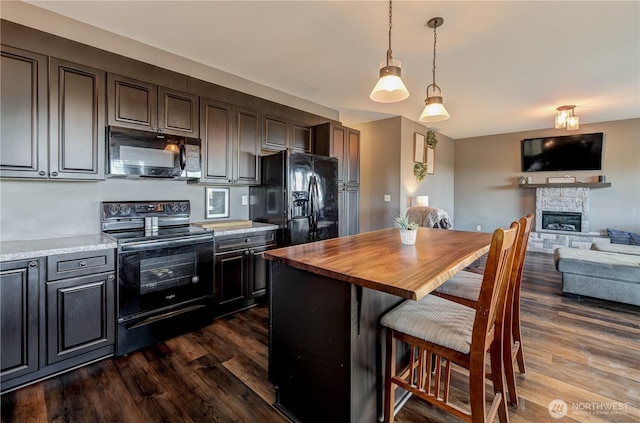 kitchen featuring open floor plan, black appliances, dark wood-type flooring, and a kitchen bar