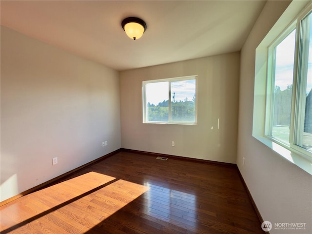 unfurnished room featuring baseboards, visible vents, and hardwood / wood-style floors