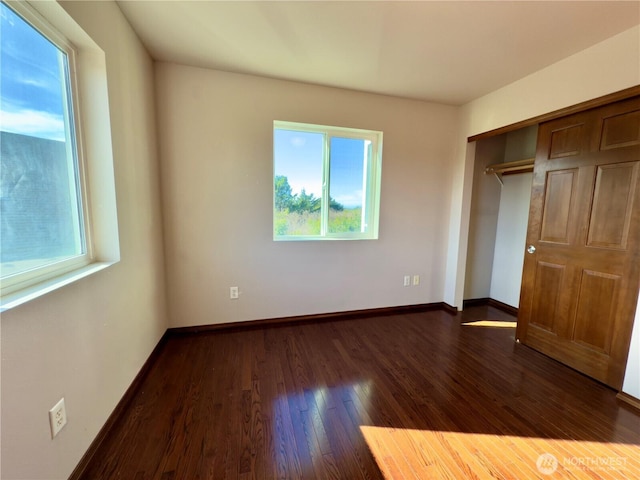 unfurnished bedroom featuring dark wood-style flooring, a closet, and baseboards