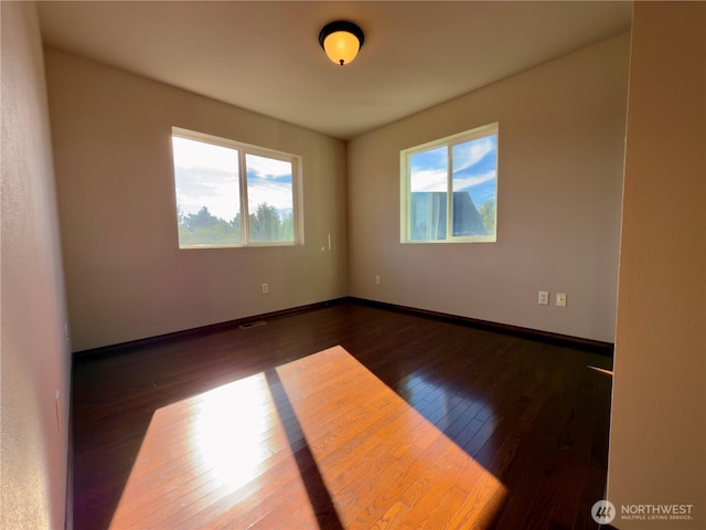 empty room featuring visible vents, wood-type flooring, a wealth of natural light, and baseboards