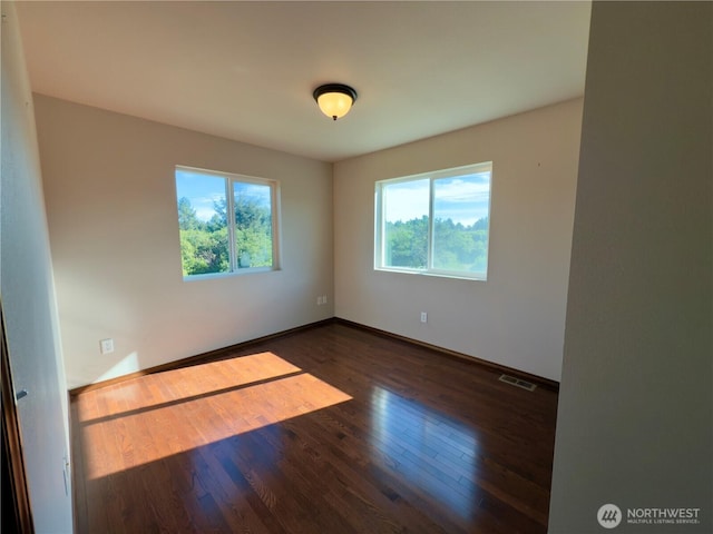 empty room with wood finished floors, visible vents, and baseboards