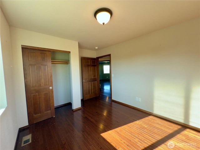 unfurnished bedroom featuring dark wood-style floors, visible vents, baseboards, and a closet