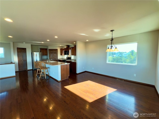 kitchen featuring dark wood finished floors, freestanding refrigerator, an island with sink, plenty of natural light, and baseboards