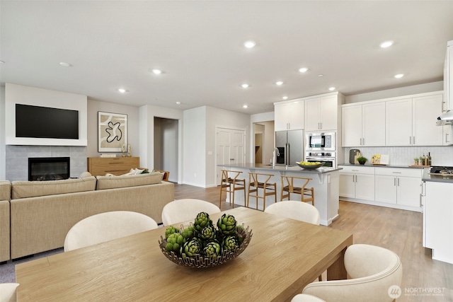 dining space featuring a tile fireplace, light wood-style flooring, and recessed lighting