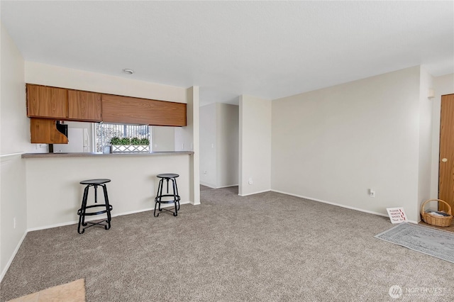 kitchen featuring a peninsula, carpet flooring, baseboards, brown cabinetry, and a kitchen bar