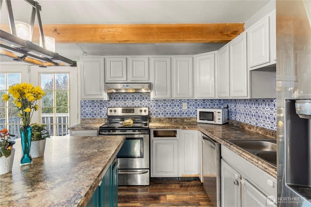 kitchen with appliances with stainless steel finishes, beamed ceiling, dark countertops, and under cabinet range hood