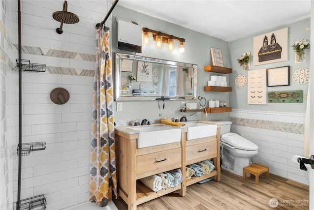 full bathroom with a wainscoted wall, wood finished floors, vanity, tile walls, and tiled shower