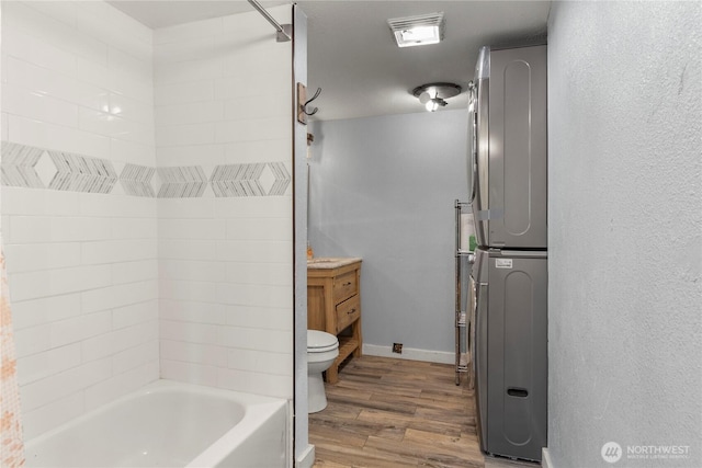 bathroom featuring toilet, stacked washer / dryer, wood finished floors, vanity, and  shower combination