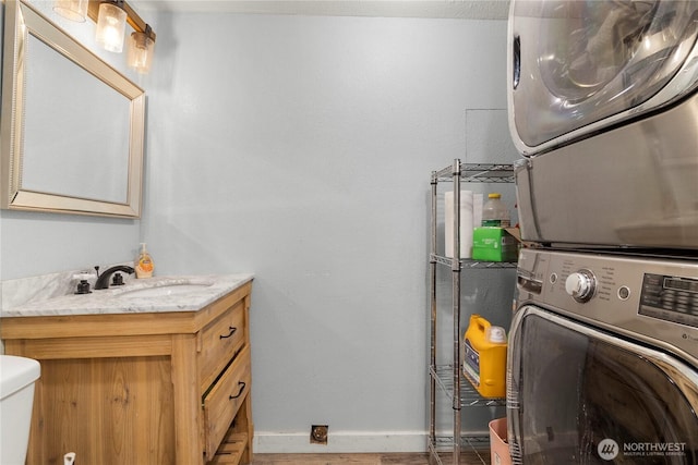 washroom with stacked washer and dryer, laundry area, a sink, and baseboards