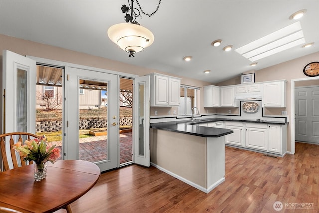 kitchen with dark countertops, white cabinets, a sink, vaulted ceiling with skylight, and a peninsula