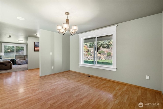 empty room featuring light wood finished floors, baseboards, visible vents, and a notable chandelier