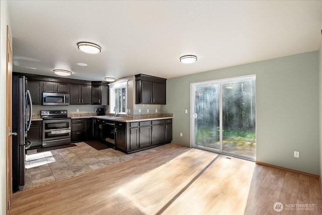 kitchen featuring stainless steel appliances, dark brown cabinets, light wood-type flooring, and a sink