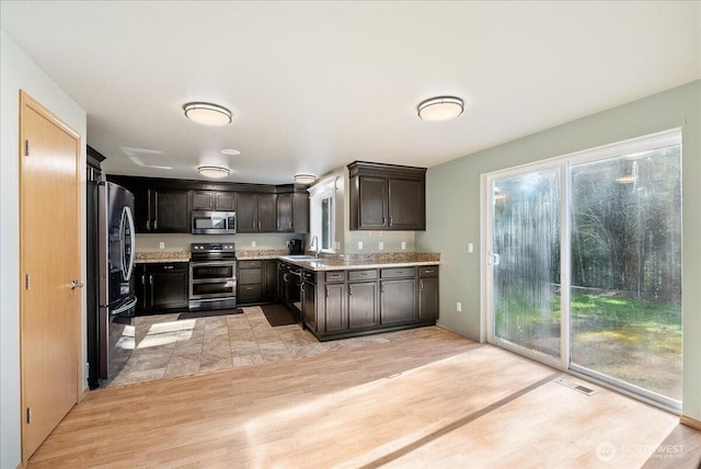 kitchen with visible vents, appliances with stainless steel finishes, a sink, dark brown cabinetry, and light wood-type flooring