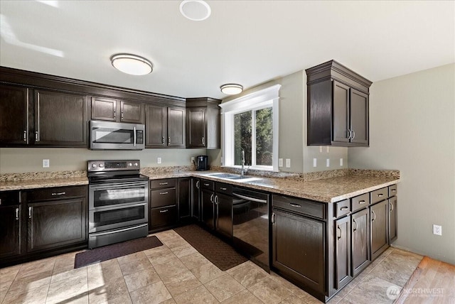 kitchen with dark brown cabinetry, light stone counters, stainless steel appliances, and a sink