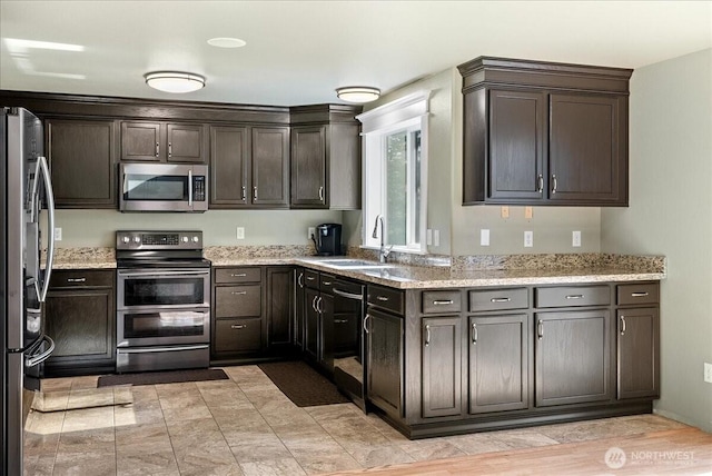 kitchen with dark brown cabinets, appliances with stainless steel finishes, a sink, and light stone countertops