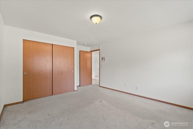 unfurnished bedroom with a closet, light carpet, and baseboards