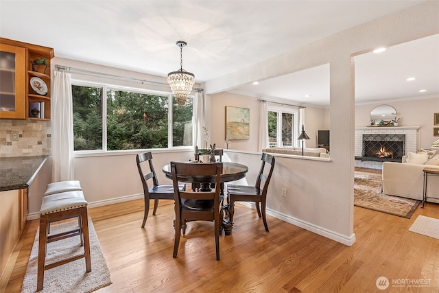 dining room featuring baseboards, light wood-type flooring, ornamental molding, recessed lighting, and a fireplace