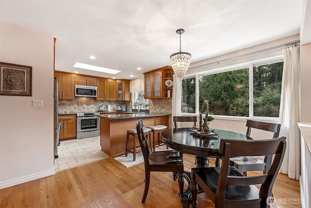 kitchen with brown cabinets, a sink, stainless steel appliances, a skylight, and decorative backsplash