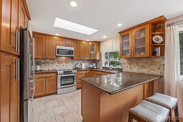 kitchen featuring brown cabinets, a peninsula, a skylight, stainless steel appliances, and a sink