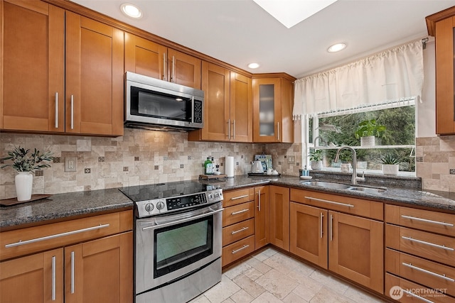 kitchen with brown cabinetry, appliances with stainless steel finishes, dark stone counters, and a sink