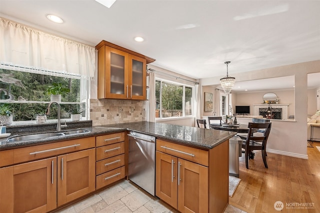 kitchen with a sink, dark stone counters, dishwasher, and brown cabinetry