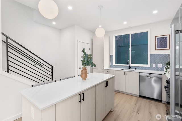 kitchen with a sink, light countertops, stainless steel dishwasher, light wood-type flooring, and backsplash