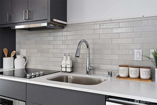 kitchen featuring dishwashing machine, black electric stovetop, under cabinet range hood, a sink, and tasteful backsplash