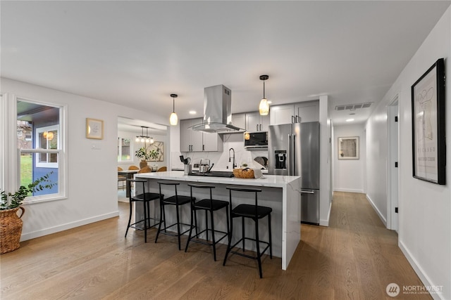 kitchen featuring a breakfast bar, light countertops, visible vents, high quality fridge, and island range hood