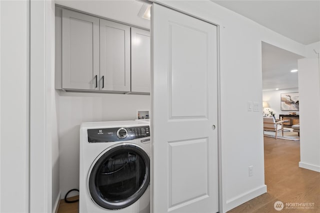 clothes washing area with baseboards, washer / clothes dryer, cabinet space, and light wood-style floors