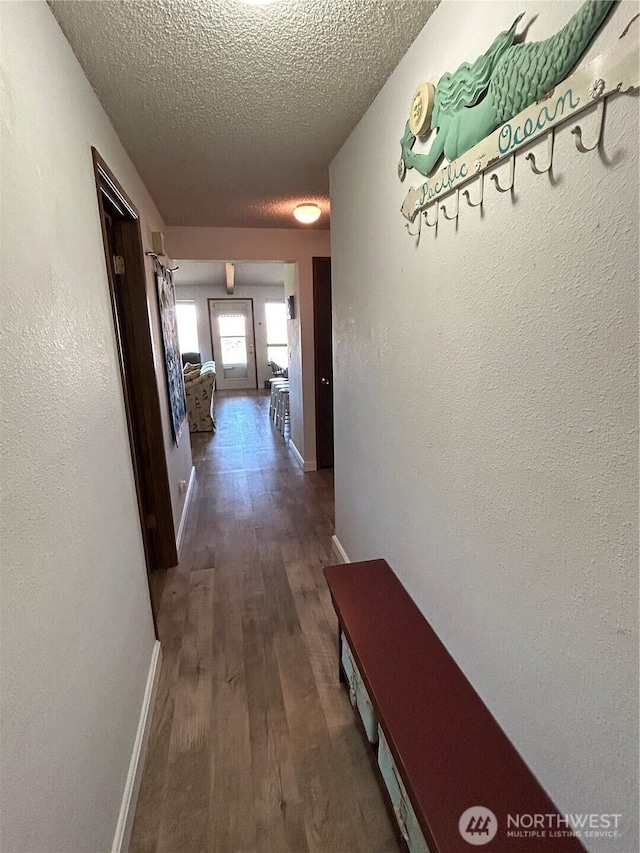 hall featuring a textured ceiling, baseboards, wood finished floors, and a textured wall