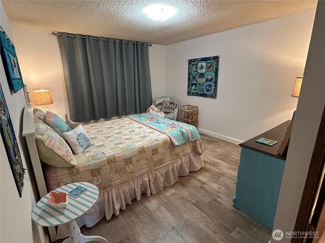 bedroom with a textured ceiling, baseboards, and wood finished floors