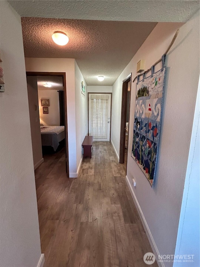 hall with a textured ceiling, baseboards, and wood finished floors