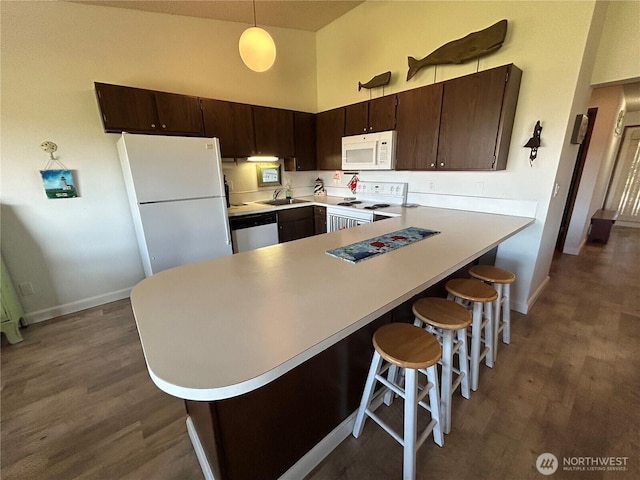 kitchen with white appliances, dark wood-style floors, a high ceiling, light countertops, and a sink