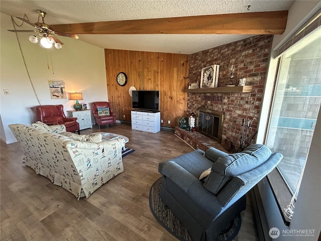 living room featuring wooden walls, wood finished floors, vaulted ceiling with beams, a textured ceiling, and a brick fireplace