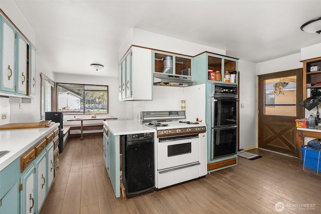 kitchen with under cabinet range hood, hardwood / wood-style floors, dobule oven black, and white range with gas cooktop