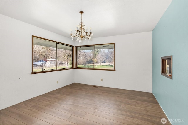 unfurnished room featuring an inviting chandelier, visible vents, and wood finished floors